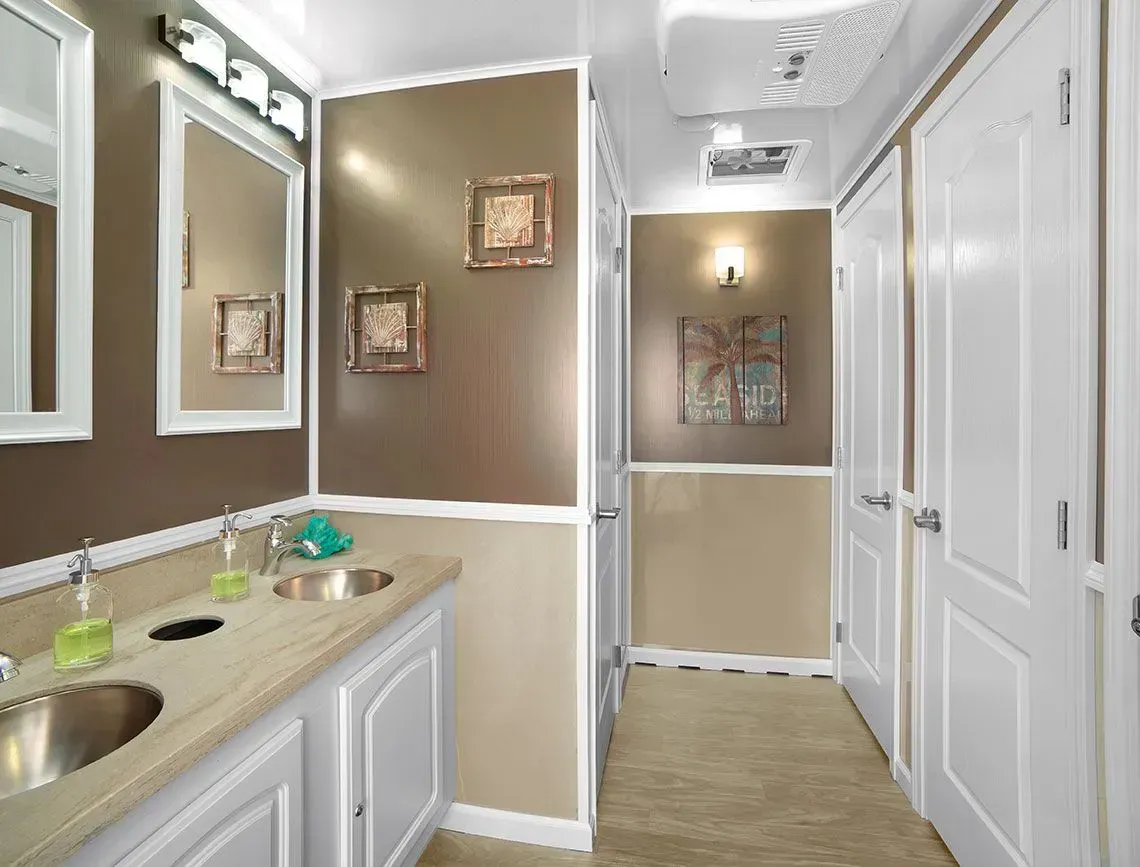 Bright bathroom with double sinks, white cabinets, brown walls, and a hallway view.