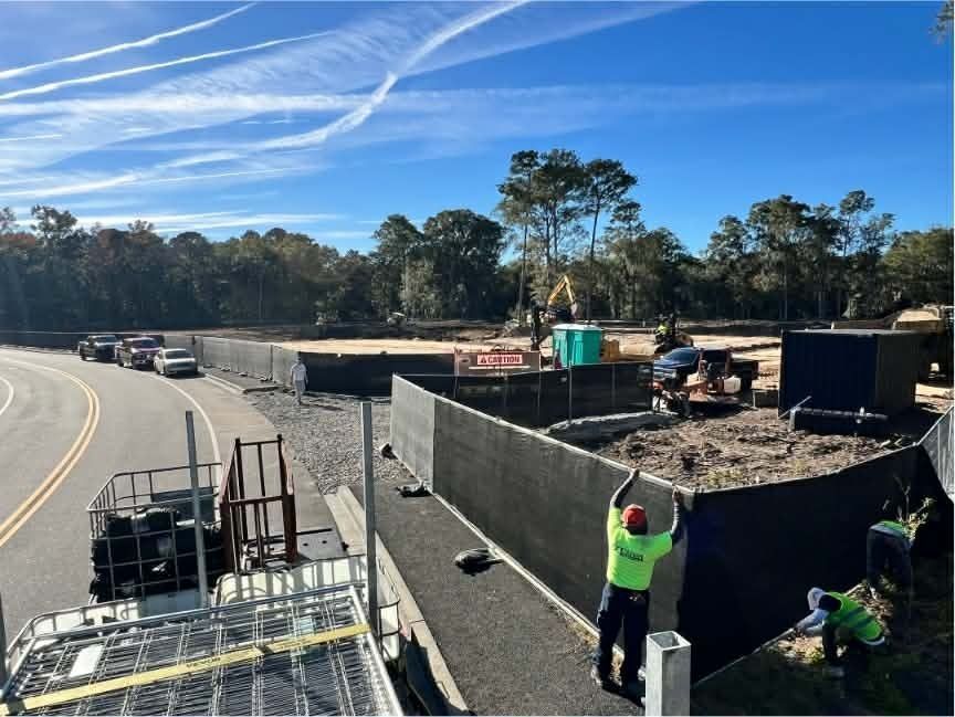 Road construction site with workers building a concrete barrier beside a highway under a blue sky