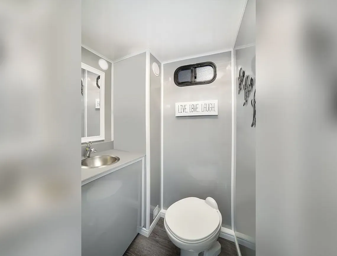 Small gray bathroom with a toilet, sink, mirror, and wall signs.