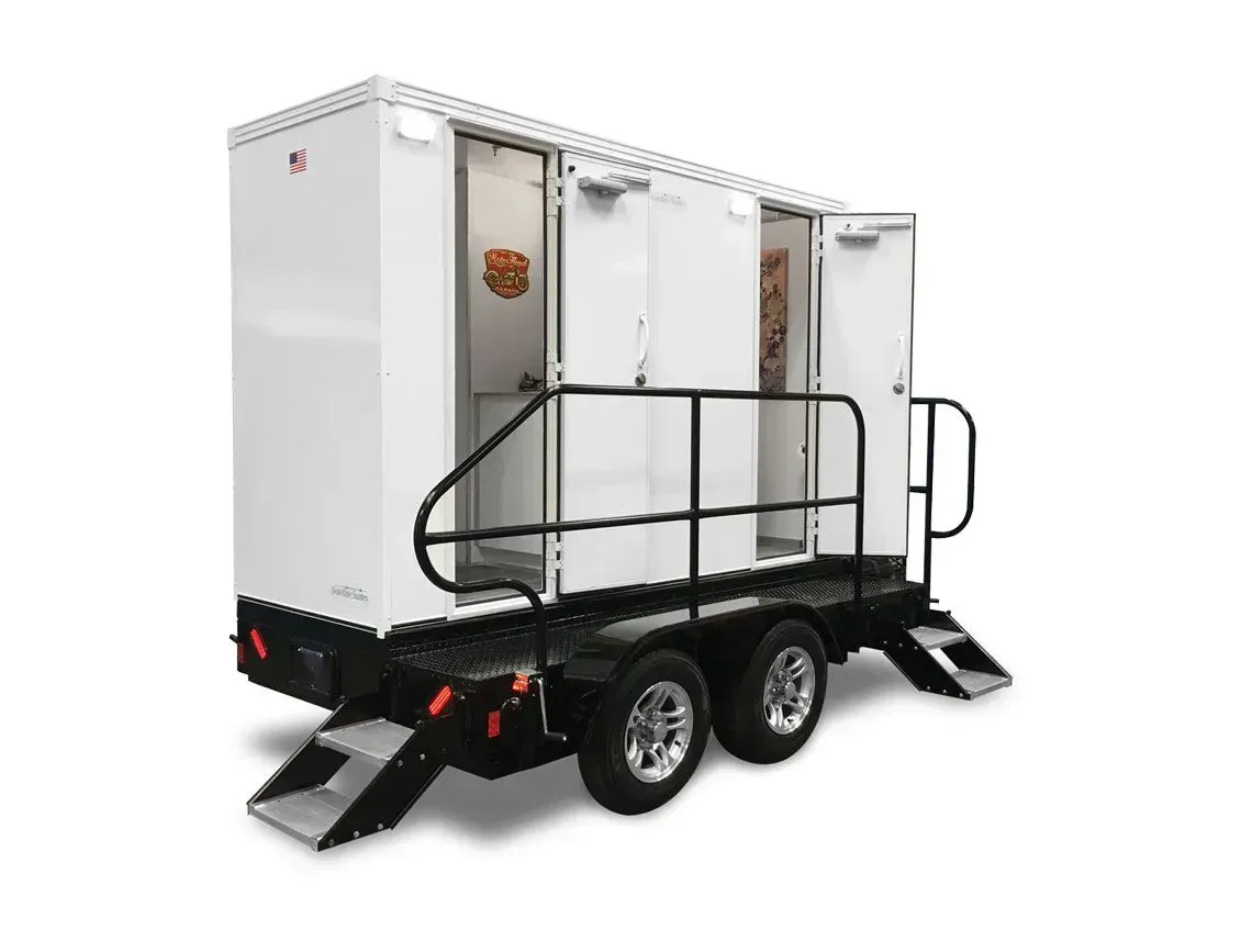 White portable restroom trailer with black railings and ramps, shown in three-quarter view.