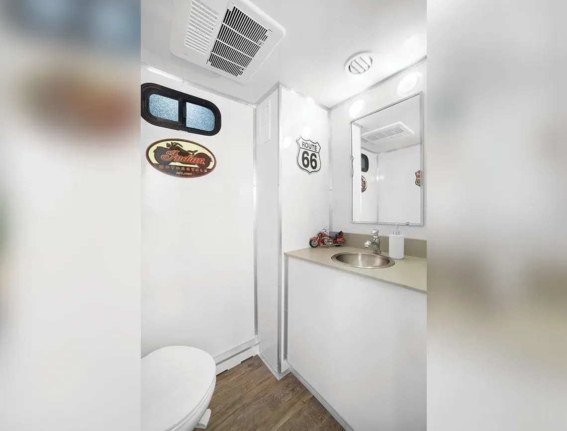 Small white bathroom with sink, mirror, toilet, and wall decor, viewed from the doorway.