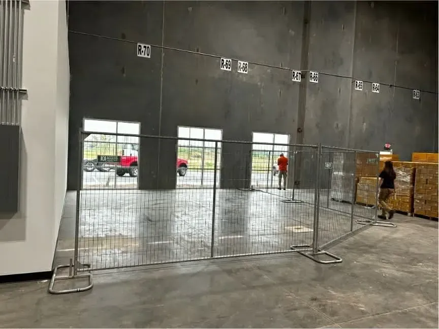 Indoor construction area with metal fencing, large black wall, and workers in the background