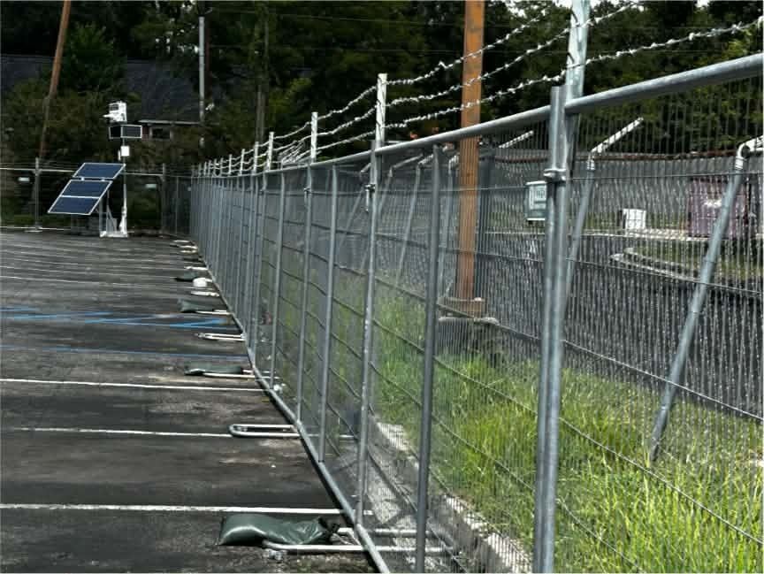 Wooden boardwalk beside a chain-link fence with solar panel in the distance, along a grassy path