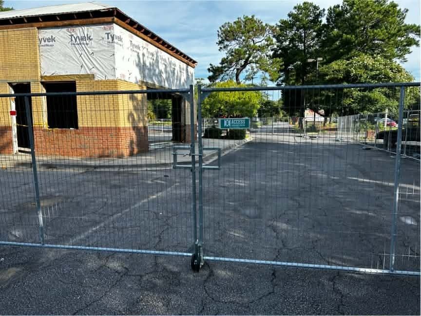 Temporary chain-link fence blocking an empty paved lot beside a brick building