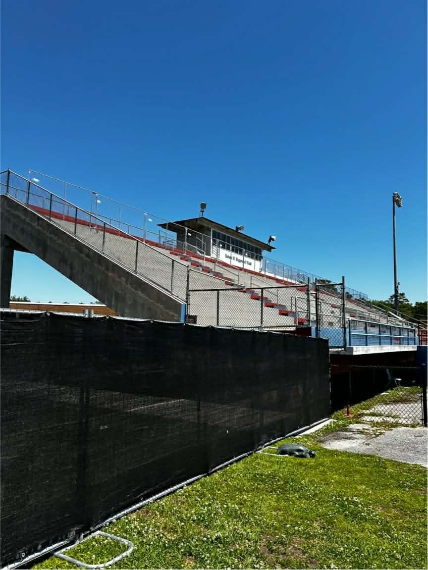 Empty outdoor grandstand with red railings behind a black fence under a clear blue sky.