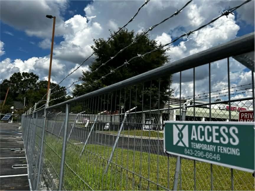Temporary construction fencing along a roadside with an ACCESS sign, grass, trees, and cloudy sky