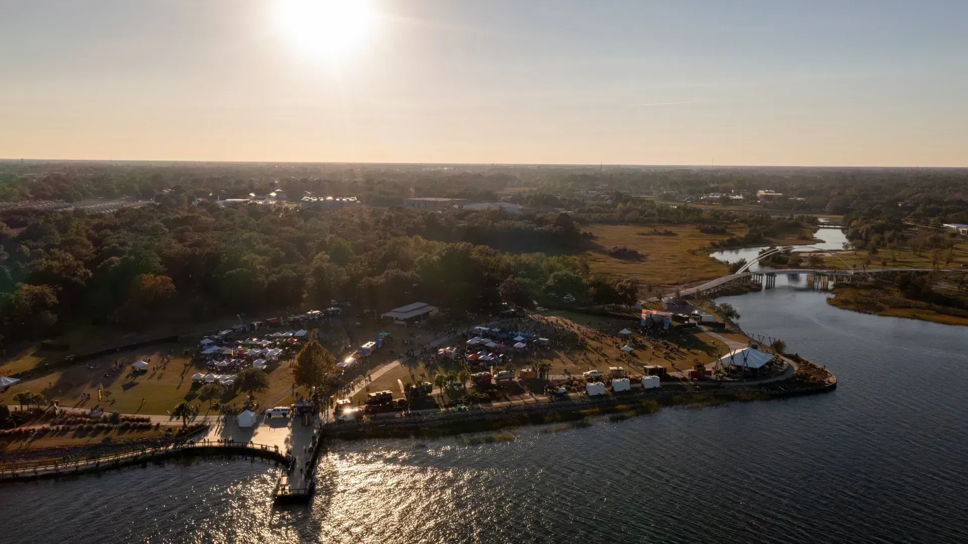Sunset aerial view of a waterfront marina, boats, and a long pier beside calm water and shoreline greenery
