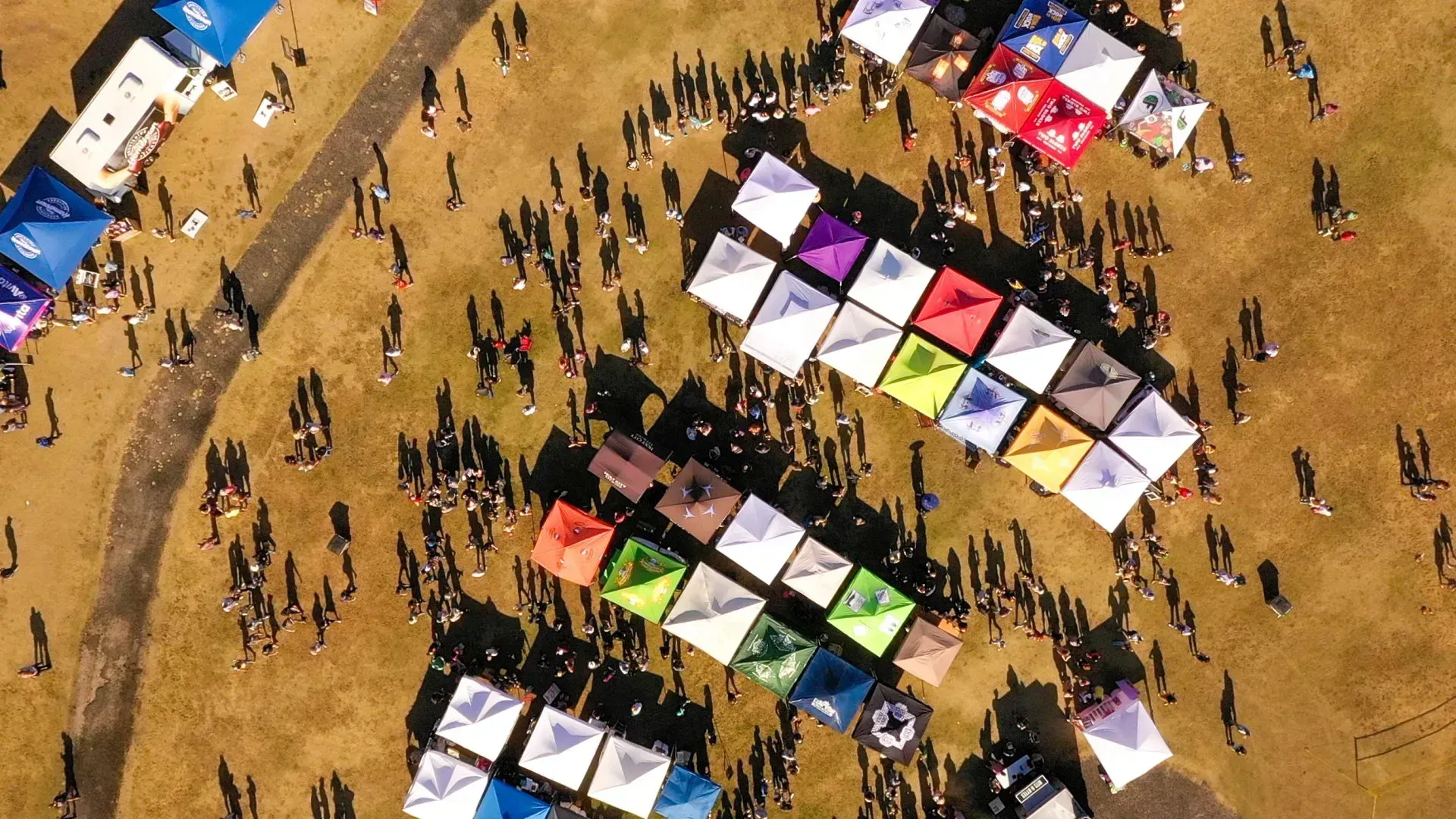 Aerial view of a crowd around rows of colorful tents on a dusty field