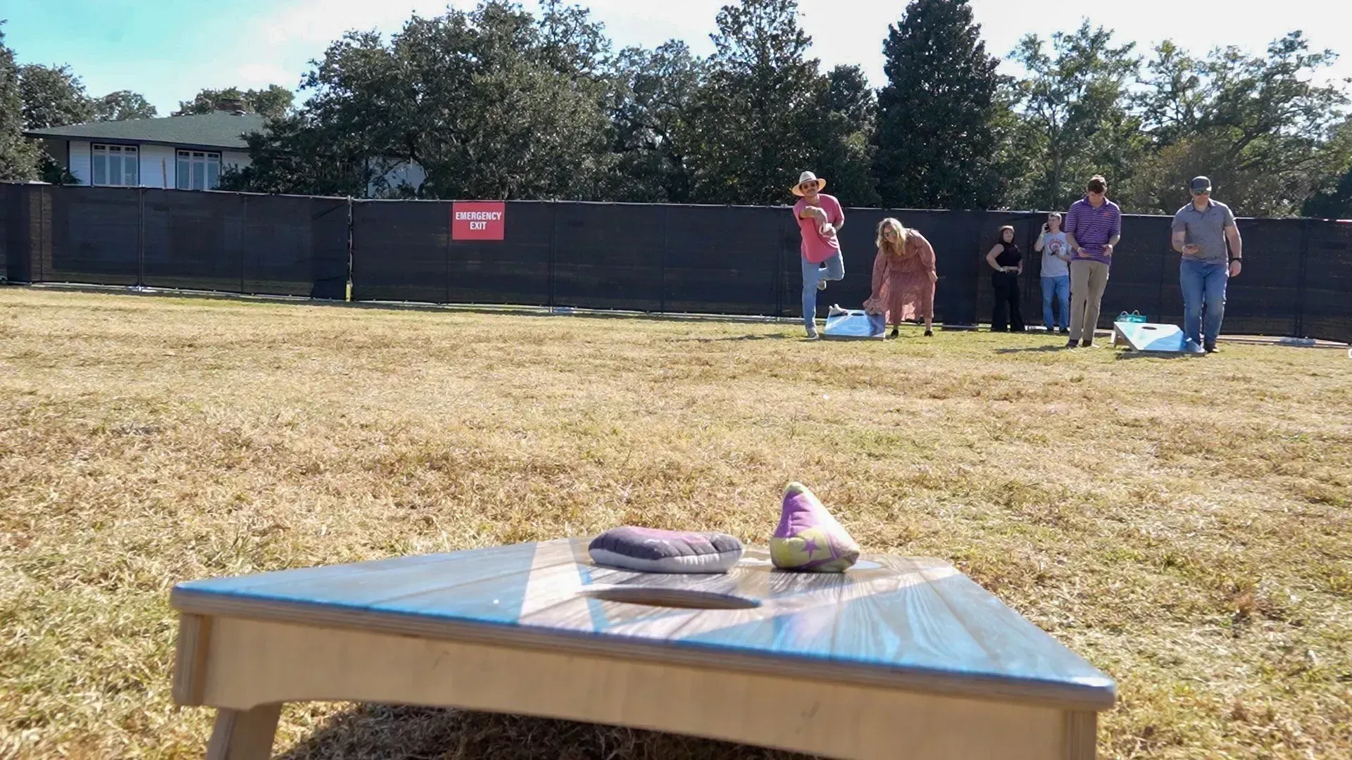 A ring toss game on a table in a sunny yard, with people standing near a fence in the background.