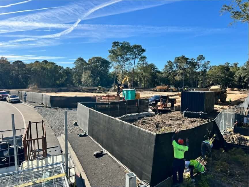 Road construction site with workers, concrete walls, equipment, and a clear blue sky