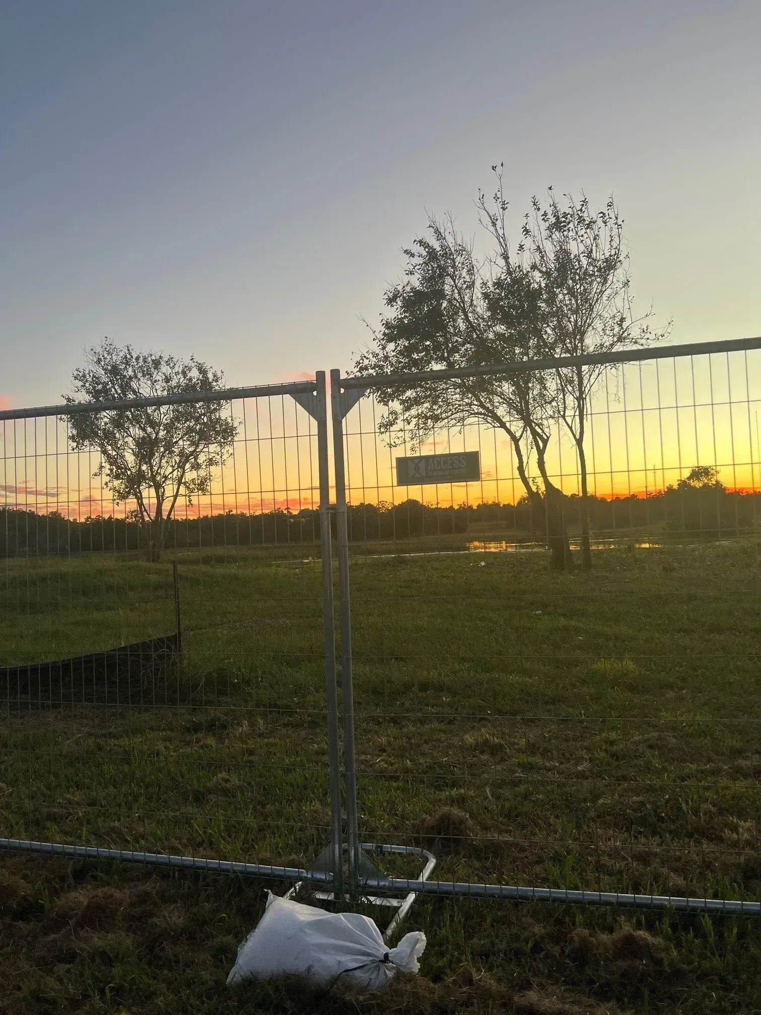 Sunset over a fenced grassy field with trees and a sign