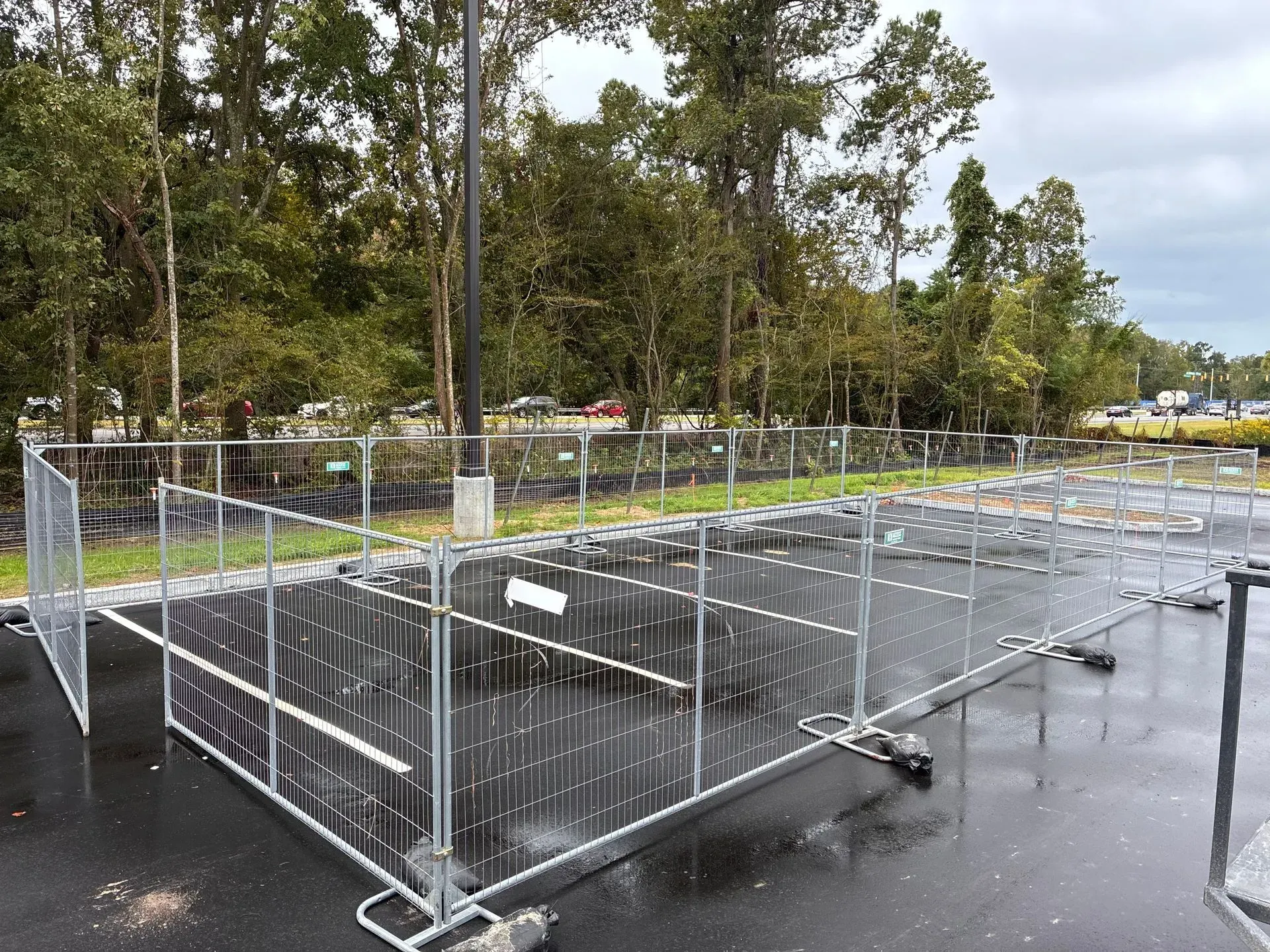 Empty metal crowd-control barricades lined up in a parking lot with trees in the background