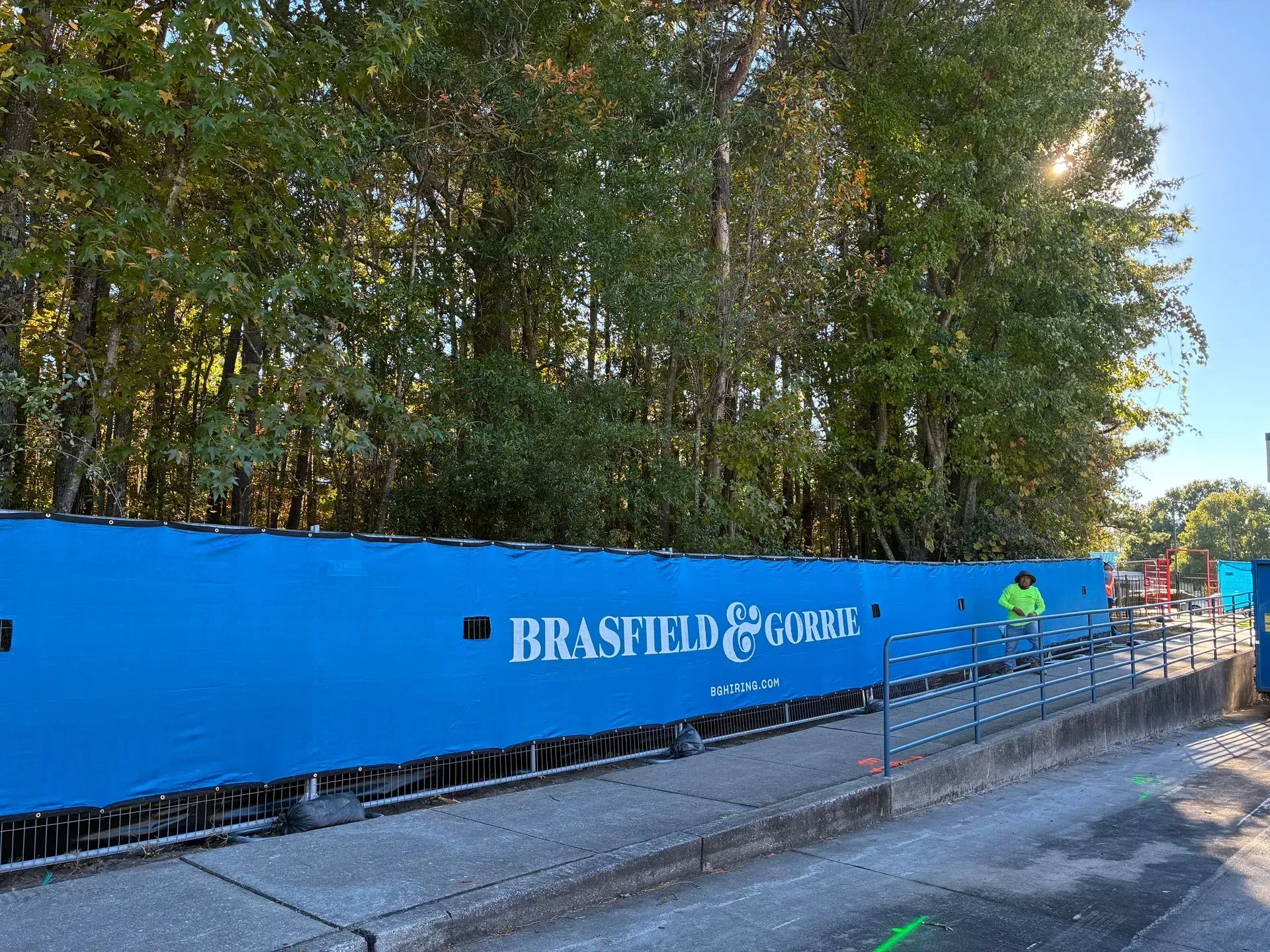Blue construction fence along a tree-lined path, with a 