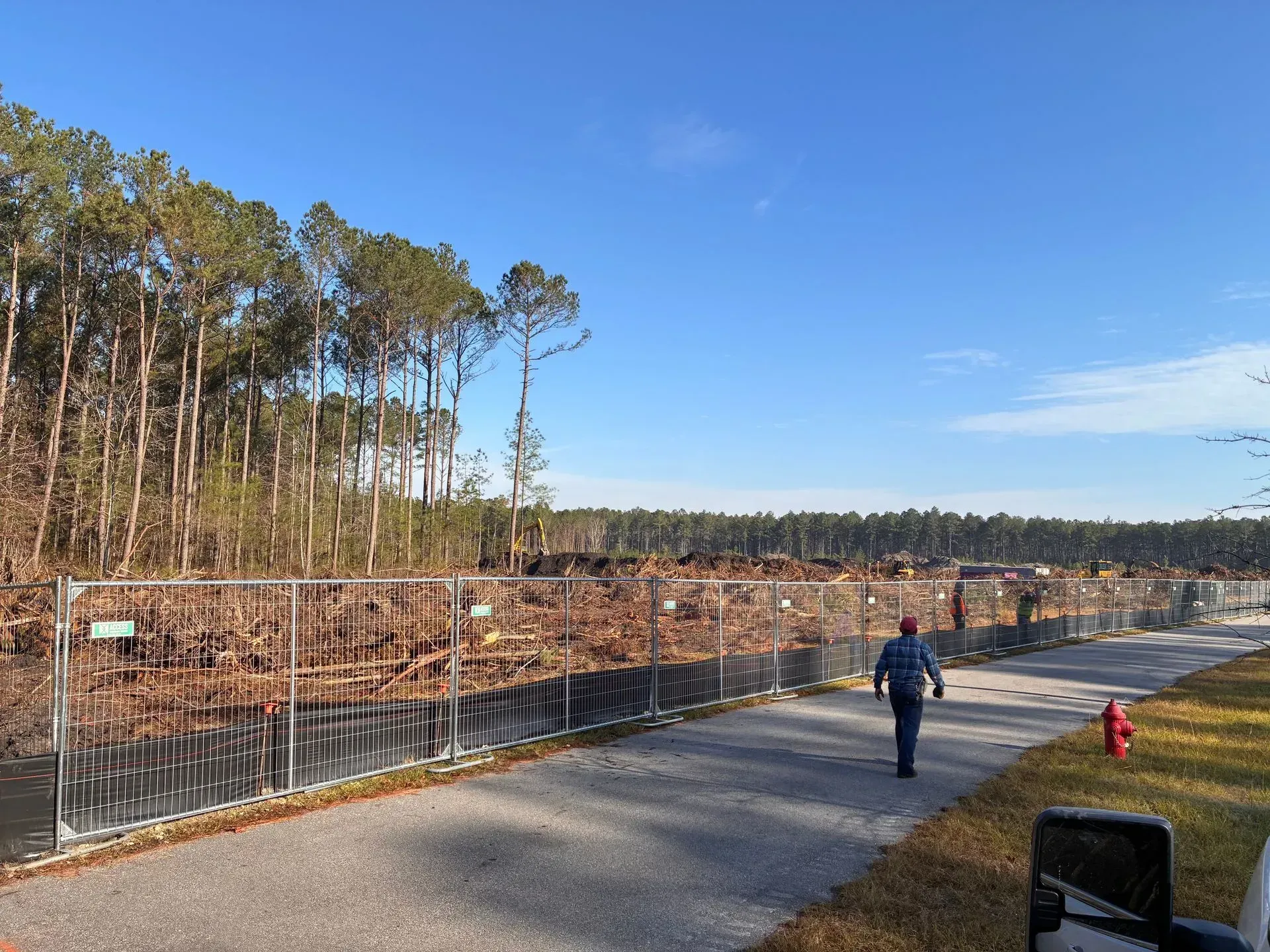 Person walking beside a fenced gravel path with a red fire hydrant, under a clear blue sky.