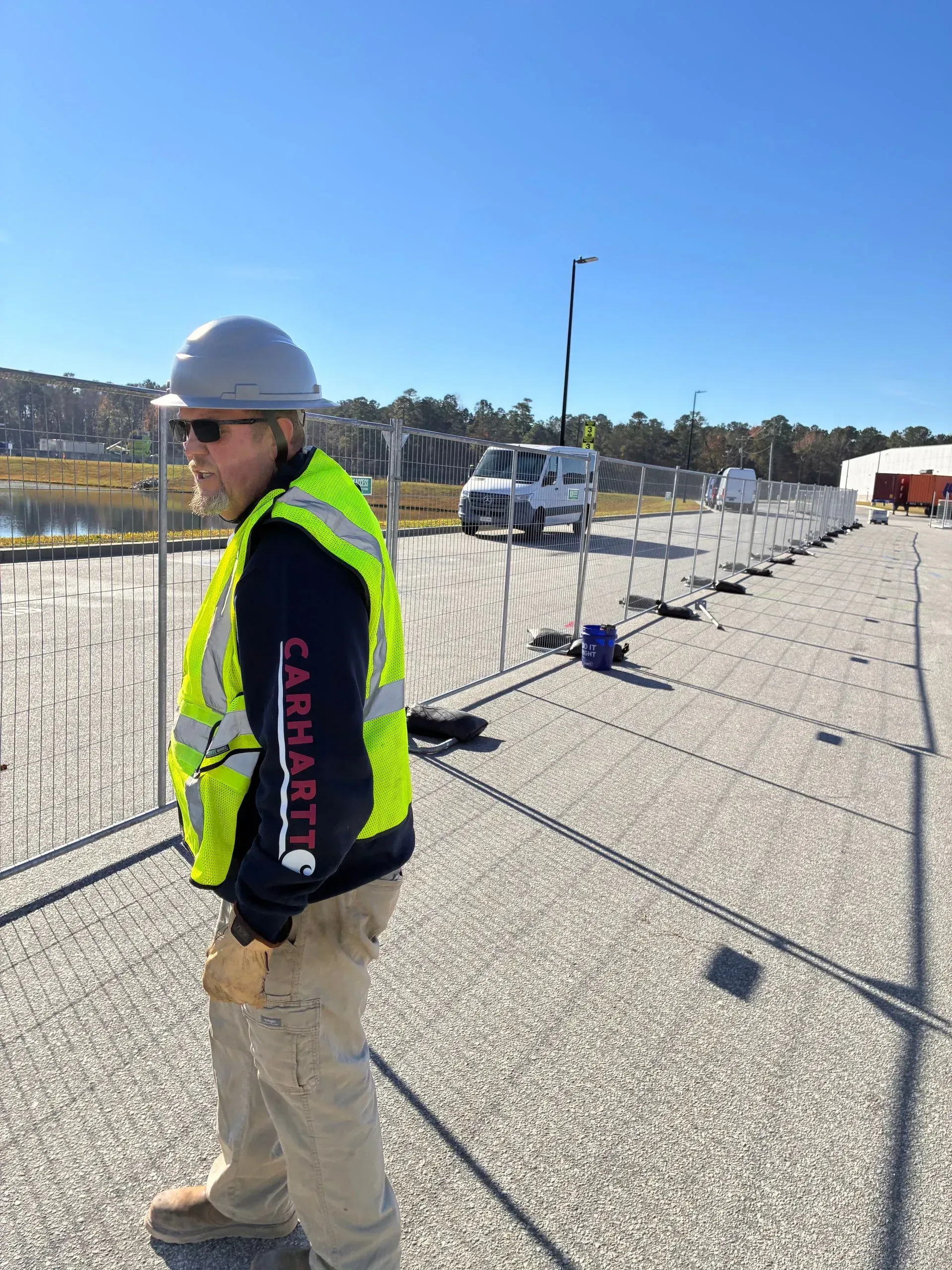 Worker in hard hat and safety vest standing on a rooftop construction site under a clear blue sky.