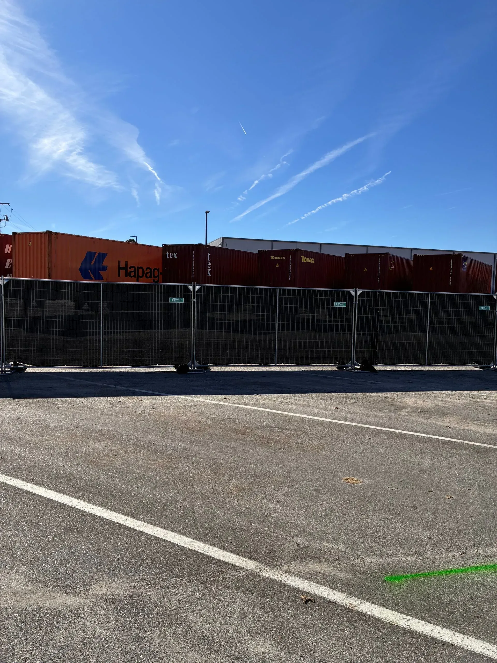 Orange shipping containers behind black fence under a bright blue sky at an industrial lot