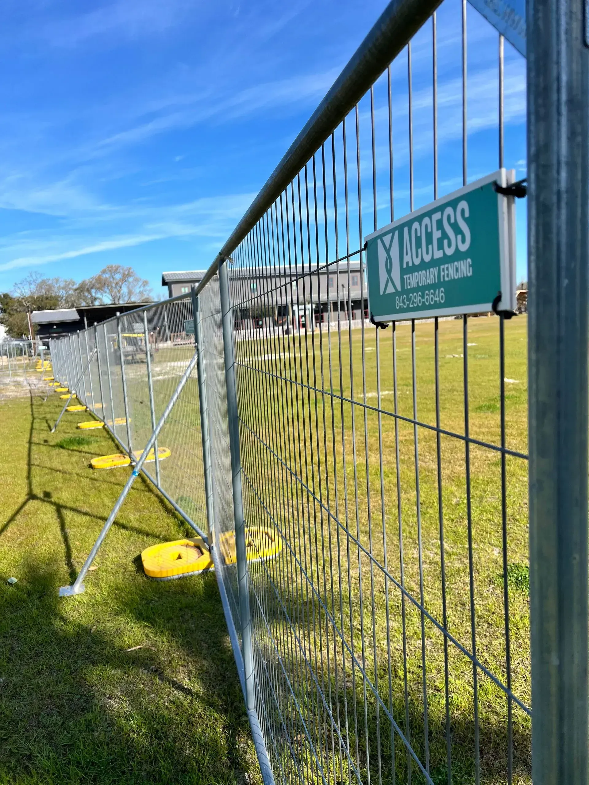 Fence-lined grassy field with a teal “ACCESS” sign under a bright blue sky