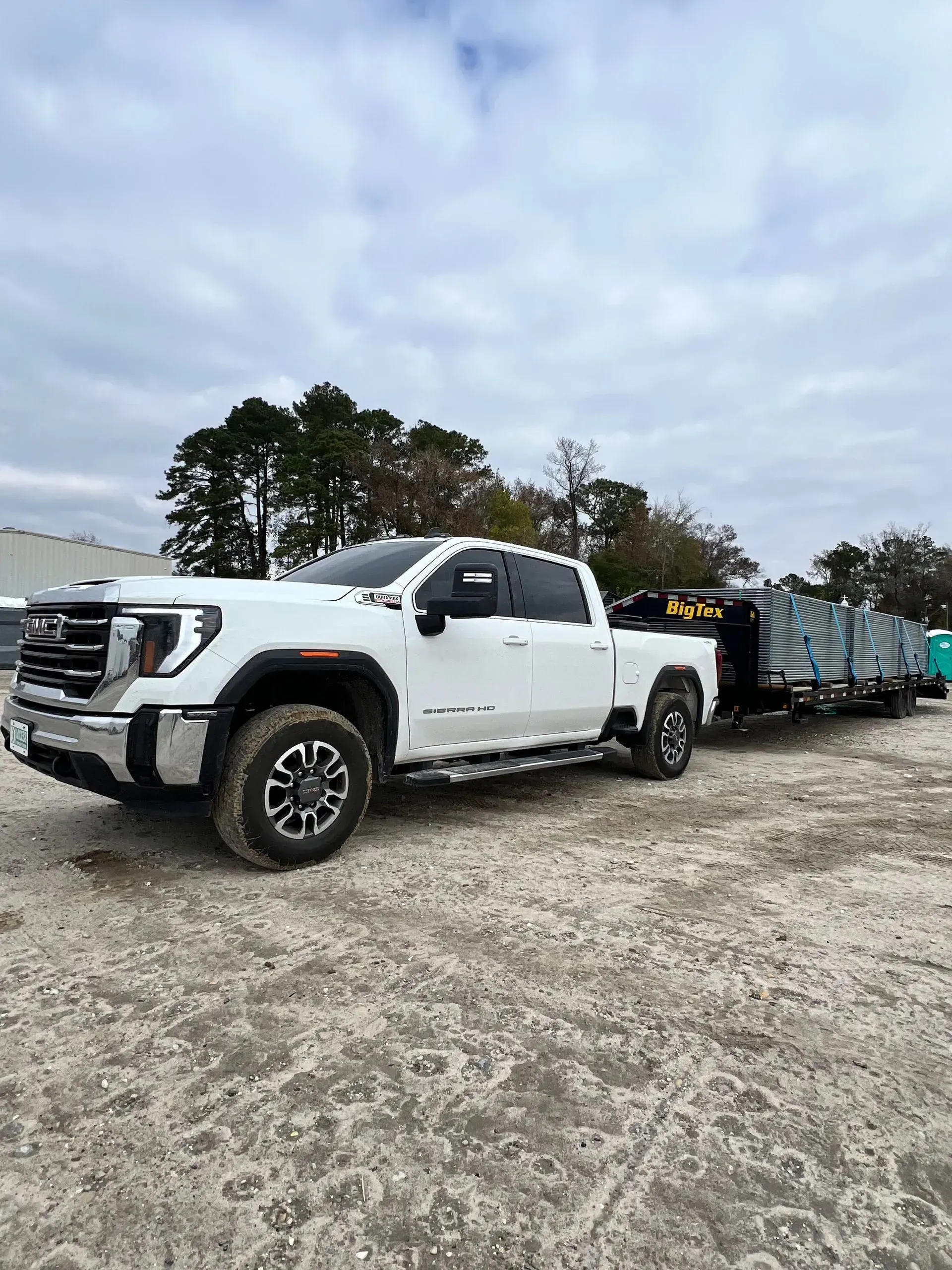 White pickup truck towing a trailer with stacked panels on a gravel lot under cloudy skies