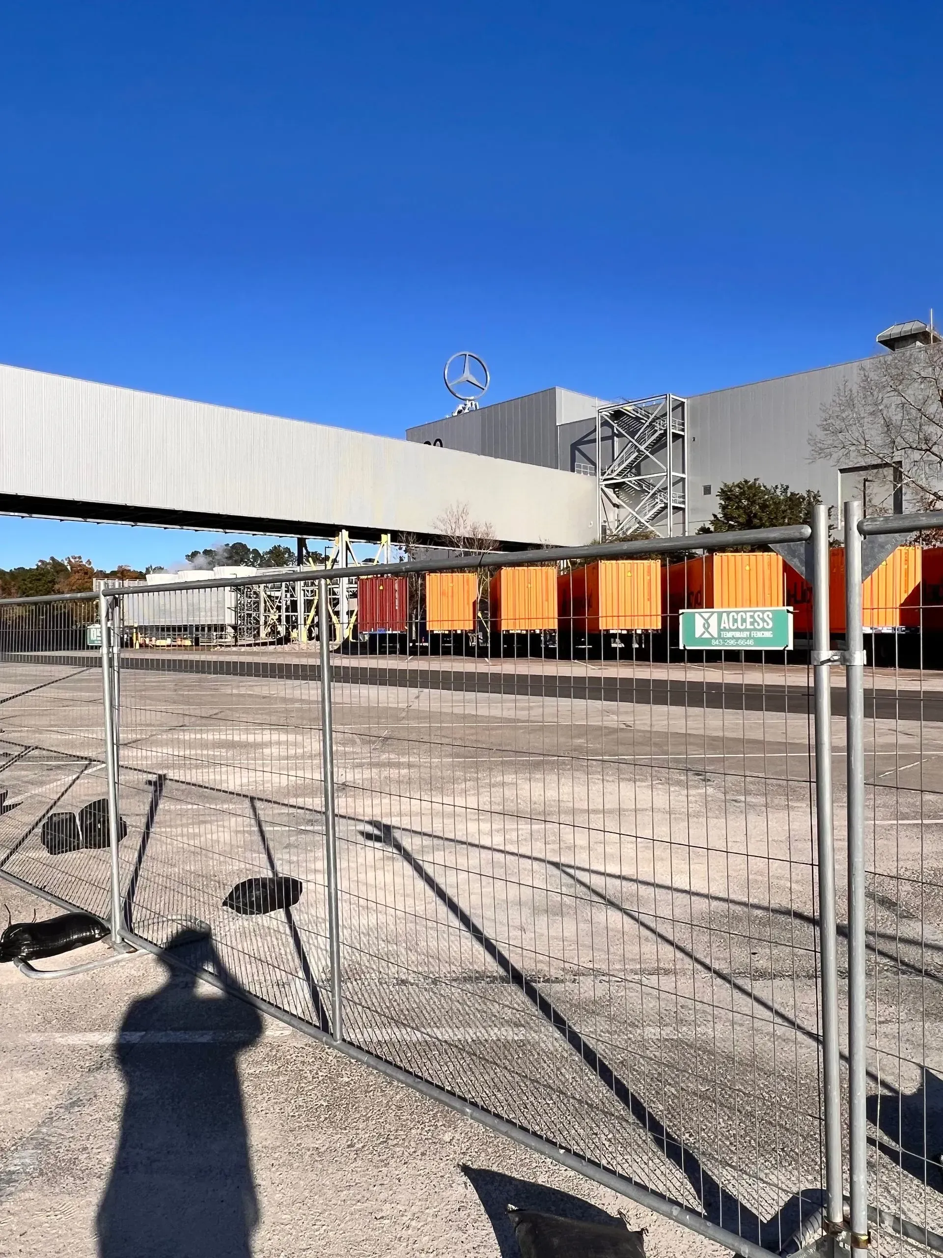 Construction site with fencing, orange containers, and a concrete overpass under a clear blue sky