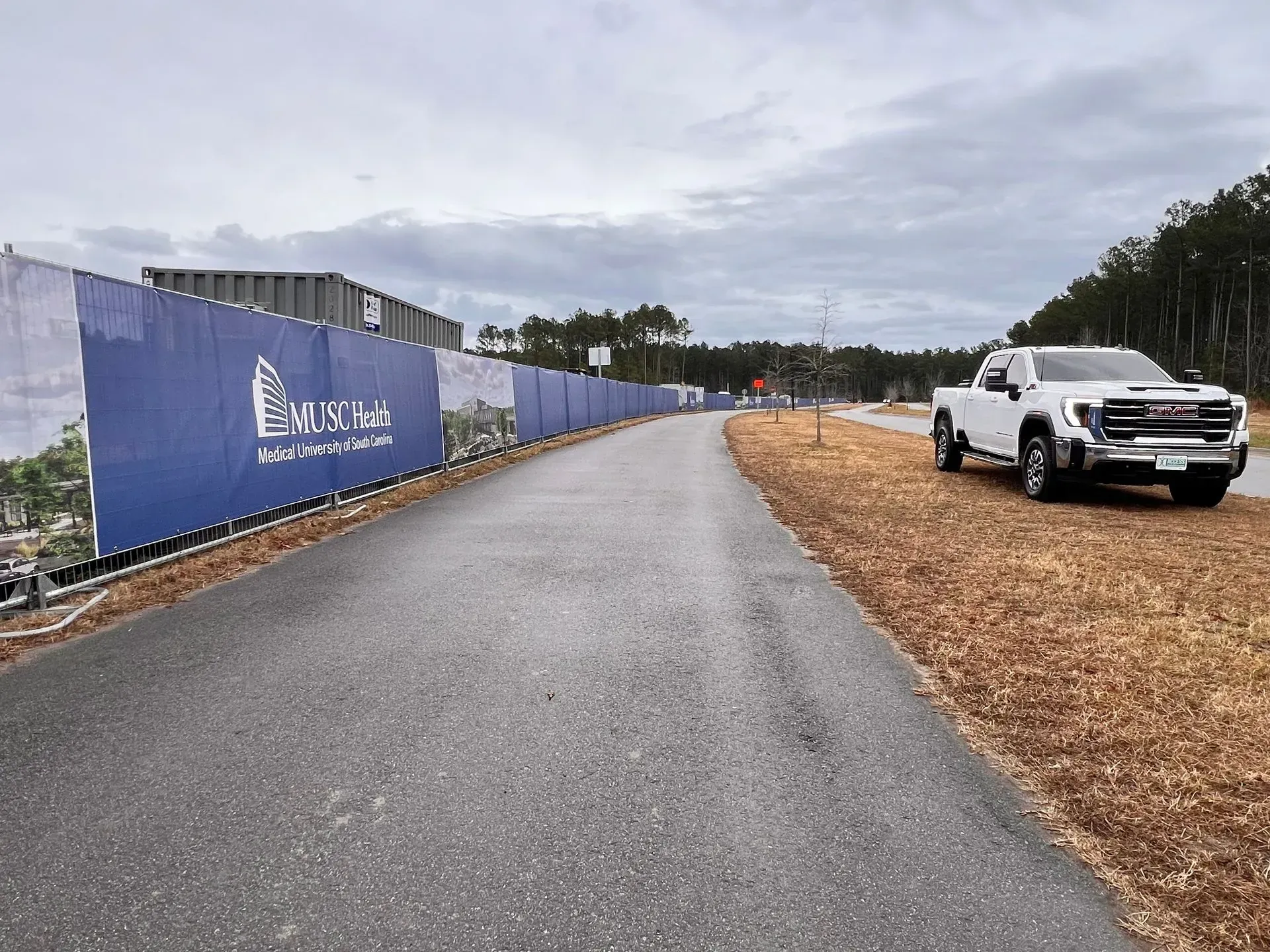 Wet paved road beside a blue construction fence, with a white pickup truck parked on the right.