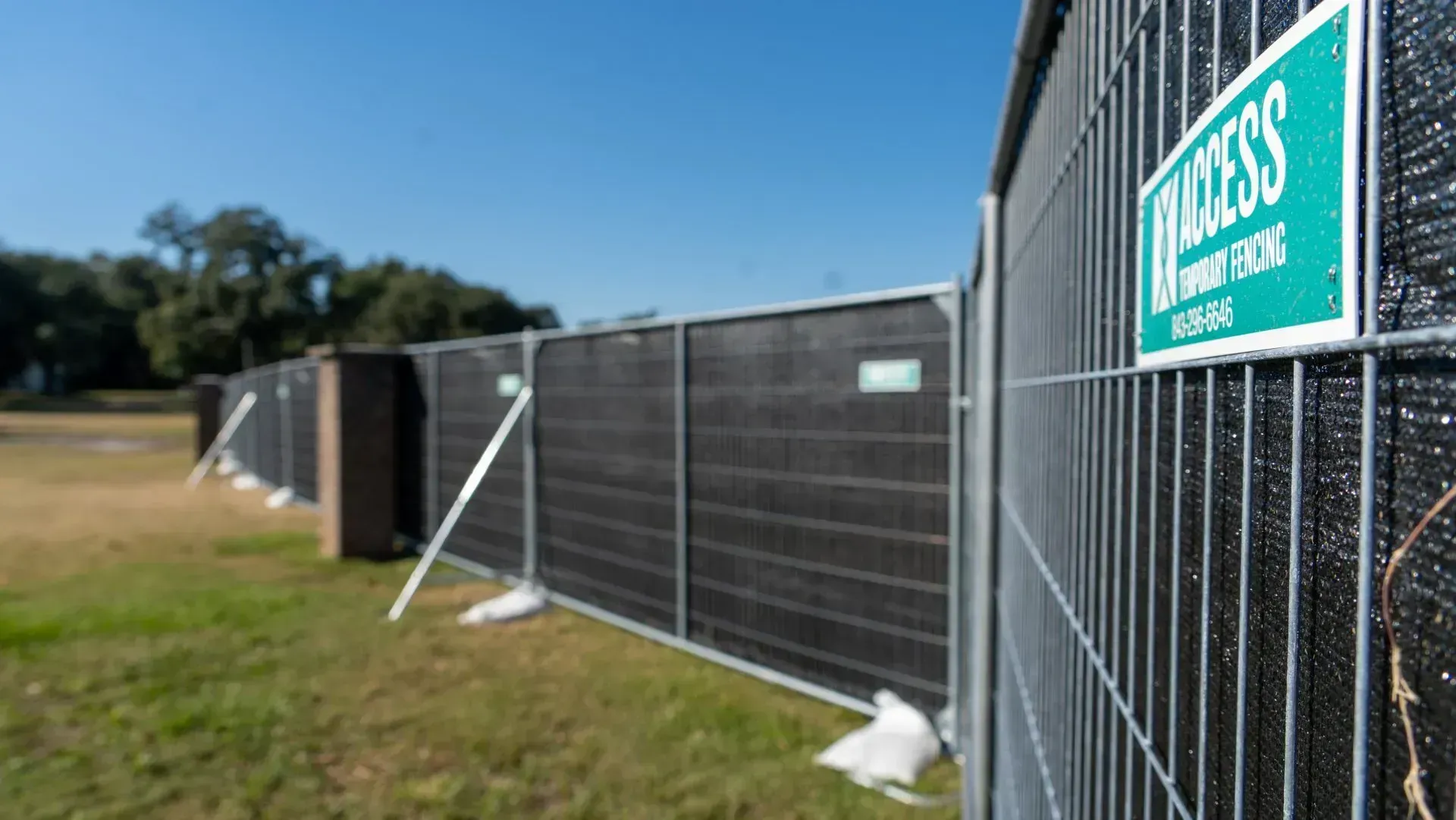 Tall black fence with a teal sign beside a grassy field on a sunny day
