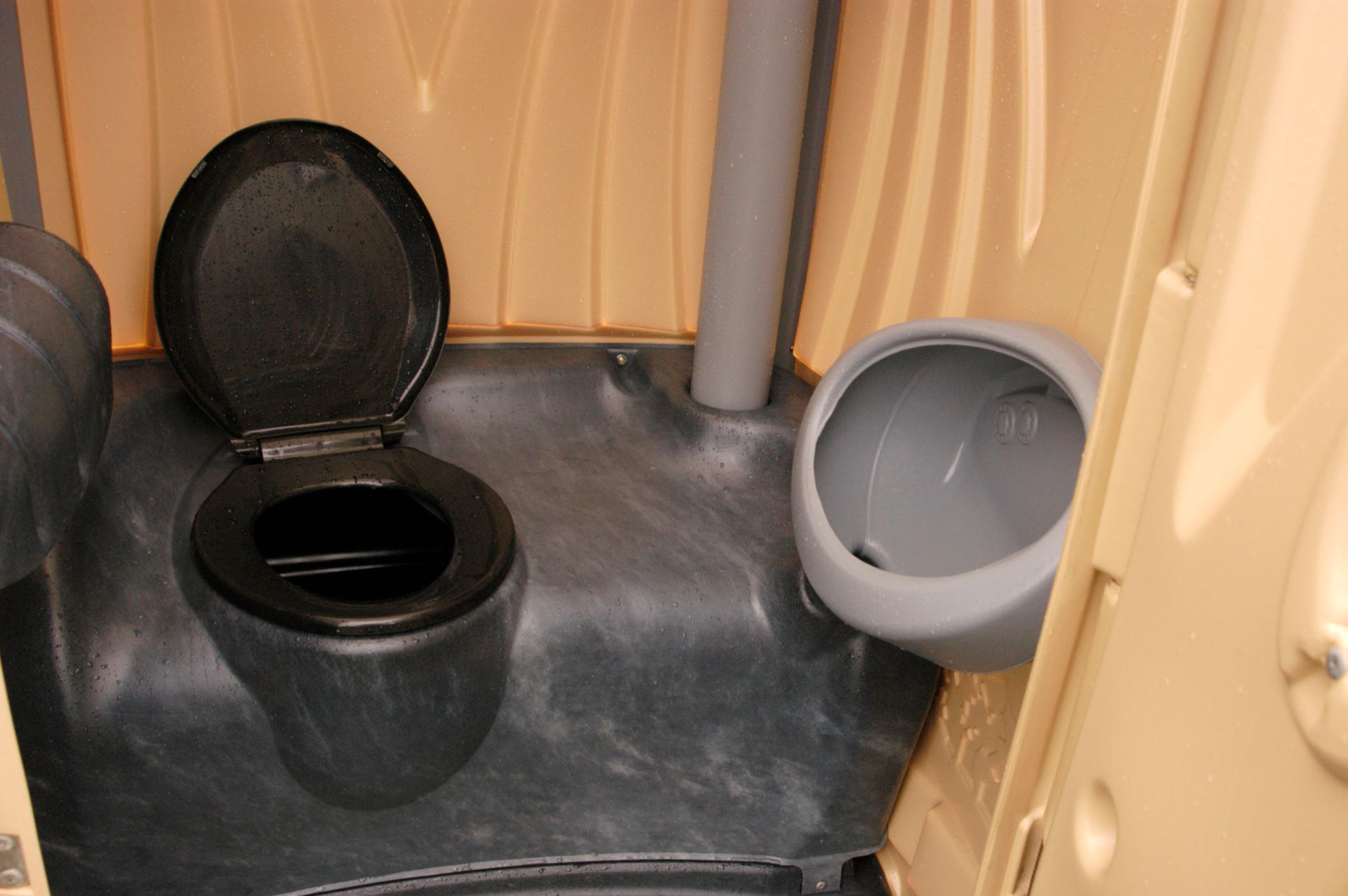 A black toilet with the lid open in a beige restroom stall, next to a gray urinal.