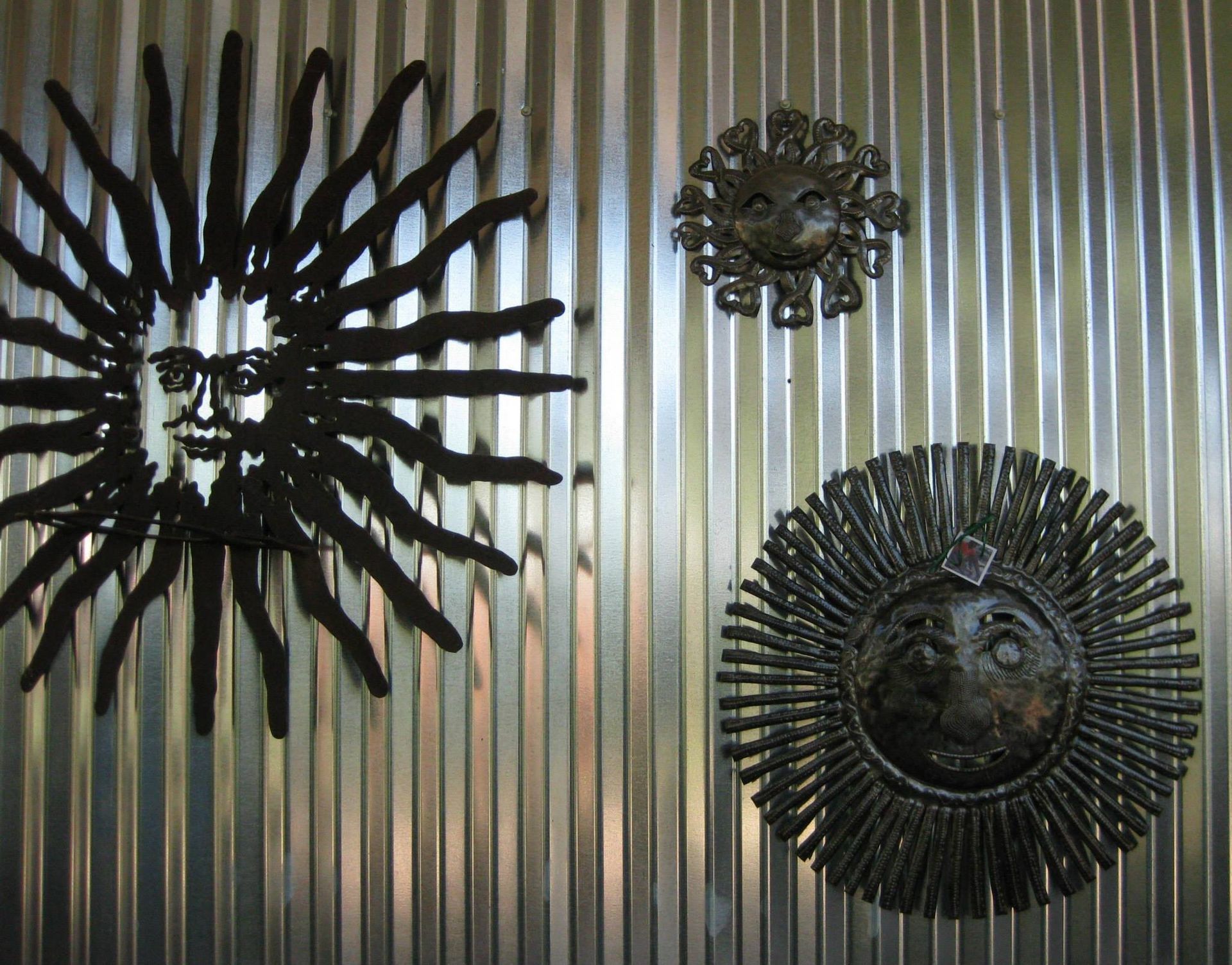 Three metal suns are hanging on a corrugated metal wall