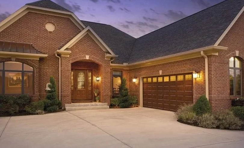 Brick home with brown door, garage, and driveway. Evening sky.