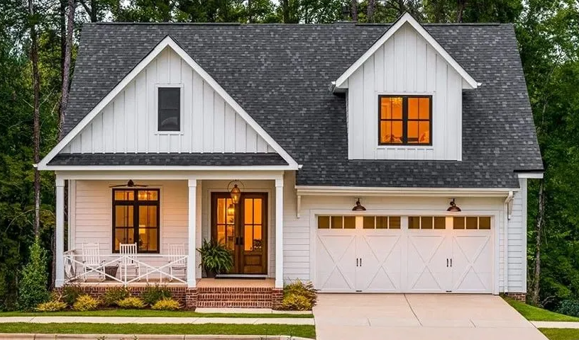White farmhouse-style home with black roof, white siding, and two-car garage. Brown doors and windows.