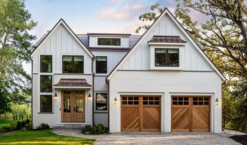 White brick and wood farmhouse with brown garage doors and trim.