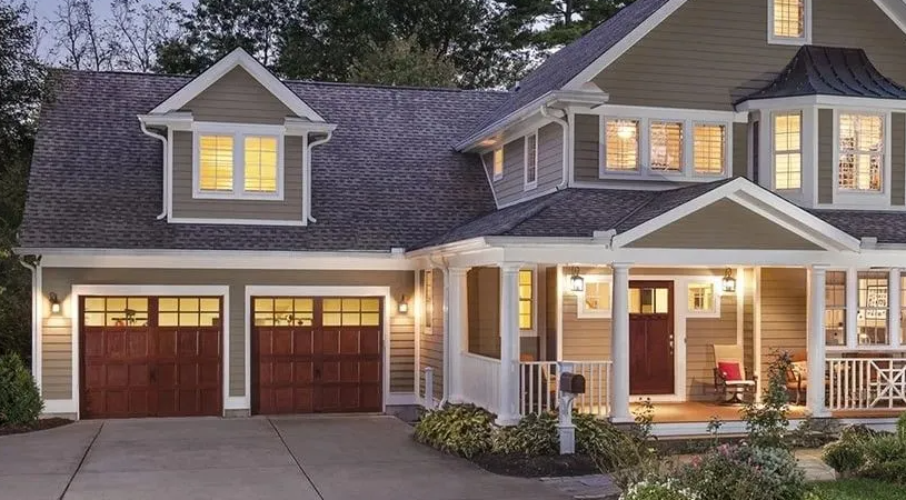 A two-story house with a porch and two-car garage, brown garage doors, tan siding, and a gray roof.