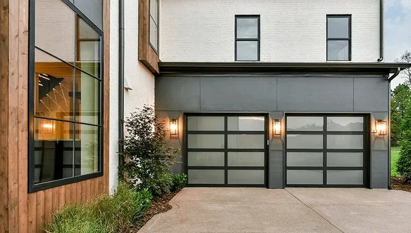 Modern home with gray garage doors, large windows, and landscaping.