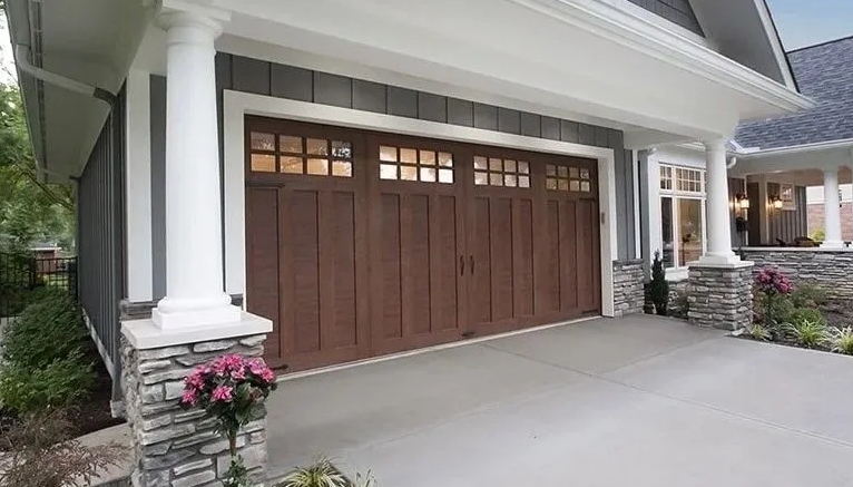 Brown garage door with glass paneling, under a white and gray exterior, flanked by stone pillars.