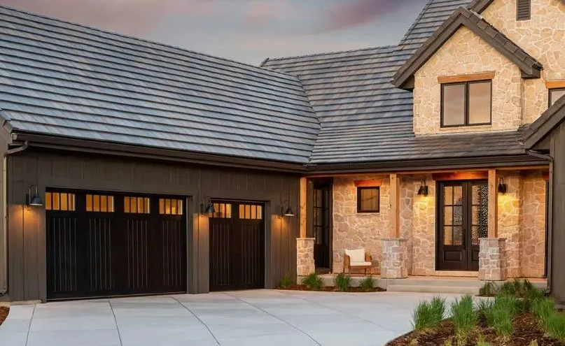 House exterior with dark garage doors, stone facade, and gray roof. Driveway and landscaping in front.