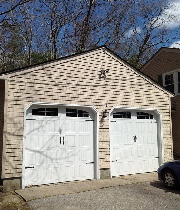 Two-car white garage with two doors, light brown shingles, black accents, and a car parked on the right.