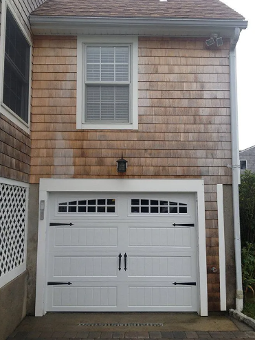 White garage door with black hardware, beneath a cedar shingle exterior with a window.