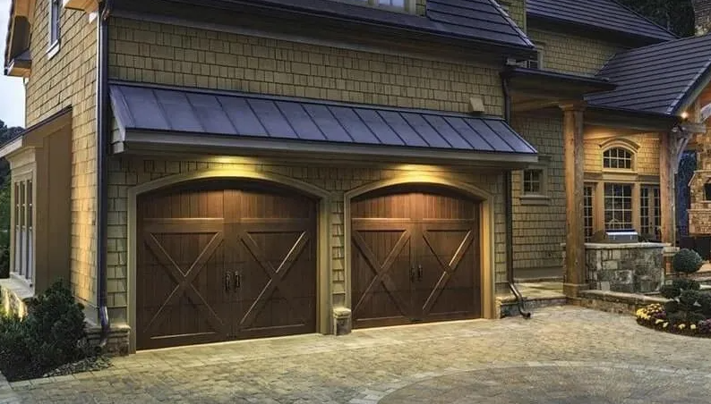 Two dark wooden garage doors with arched tops under a metal awning. Evening lighting illuminates the doors.