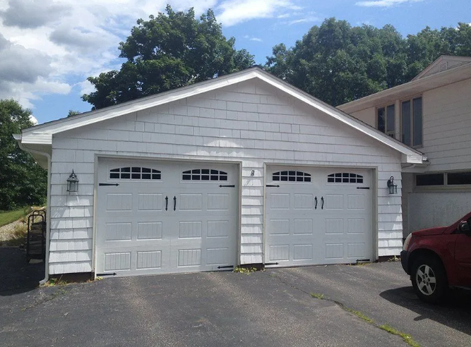 White two-car garage with two doors. White siding, black asphalt driveway. Red SUV parked on right.