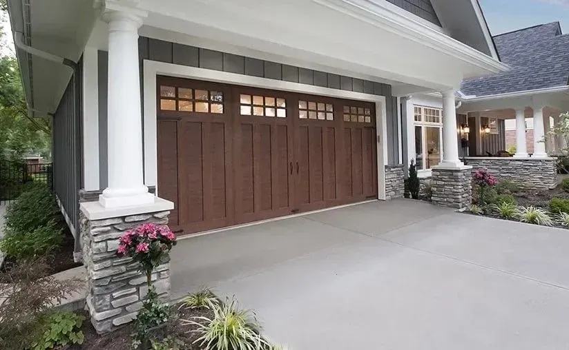 Brown garage door with windows, flanked by white columns, concrete driveway, and stone accents.
