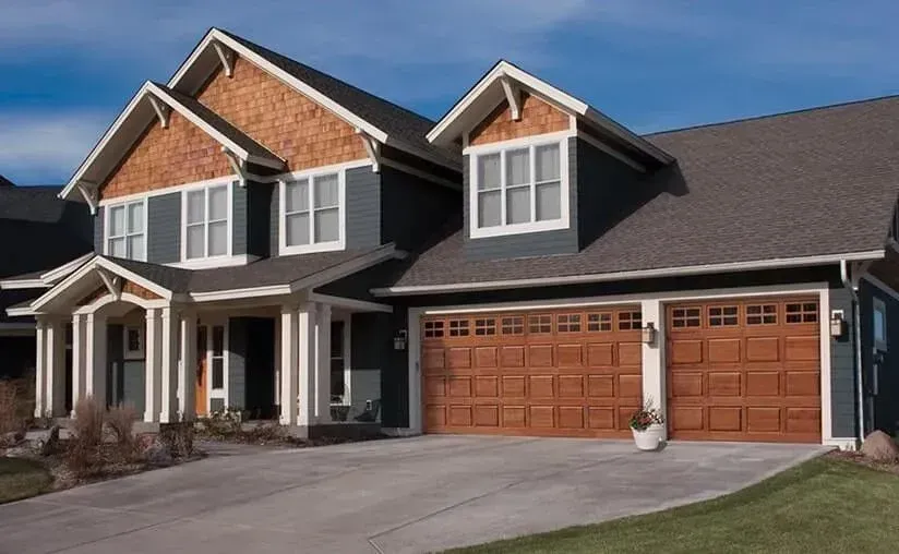 Two-story blue house with brown roof and garage doors, white trim. Driveway and grass in front.