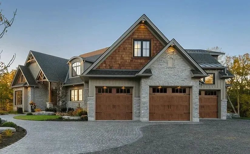 Three-car garage of a stone and wood house with a long, gray driveway.