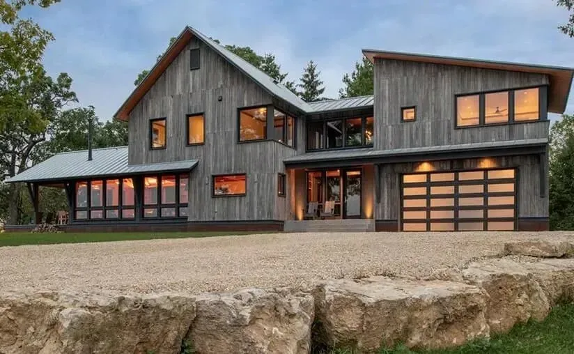 Gray weathered wood house with modern design features, including large windows and a gravel driveway.
