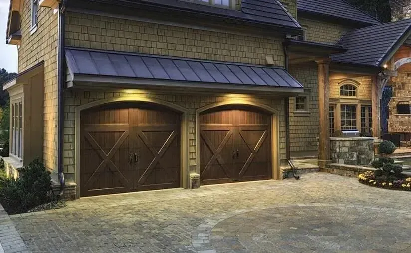 Brown wooden garage doors on a house with a stone and shingle exterior, lit driveway.