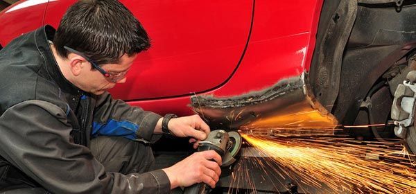 A man is grinding a red car with a grinder.