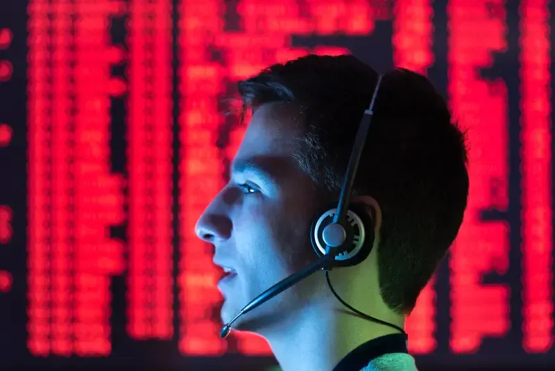 Man with headset in front of a red screen, looking to the side, illuminated by blue and red light.