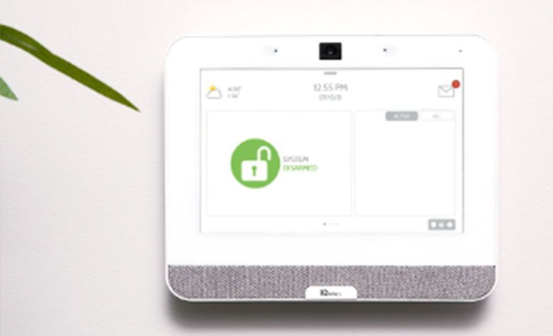 White security system panel mounted on a wall, displaying a green unlocked lock icon and other system information.
