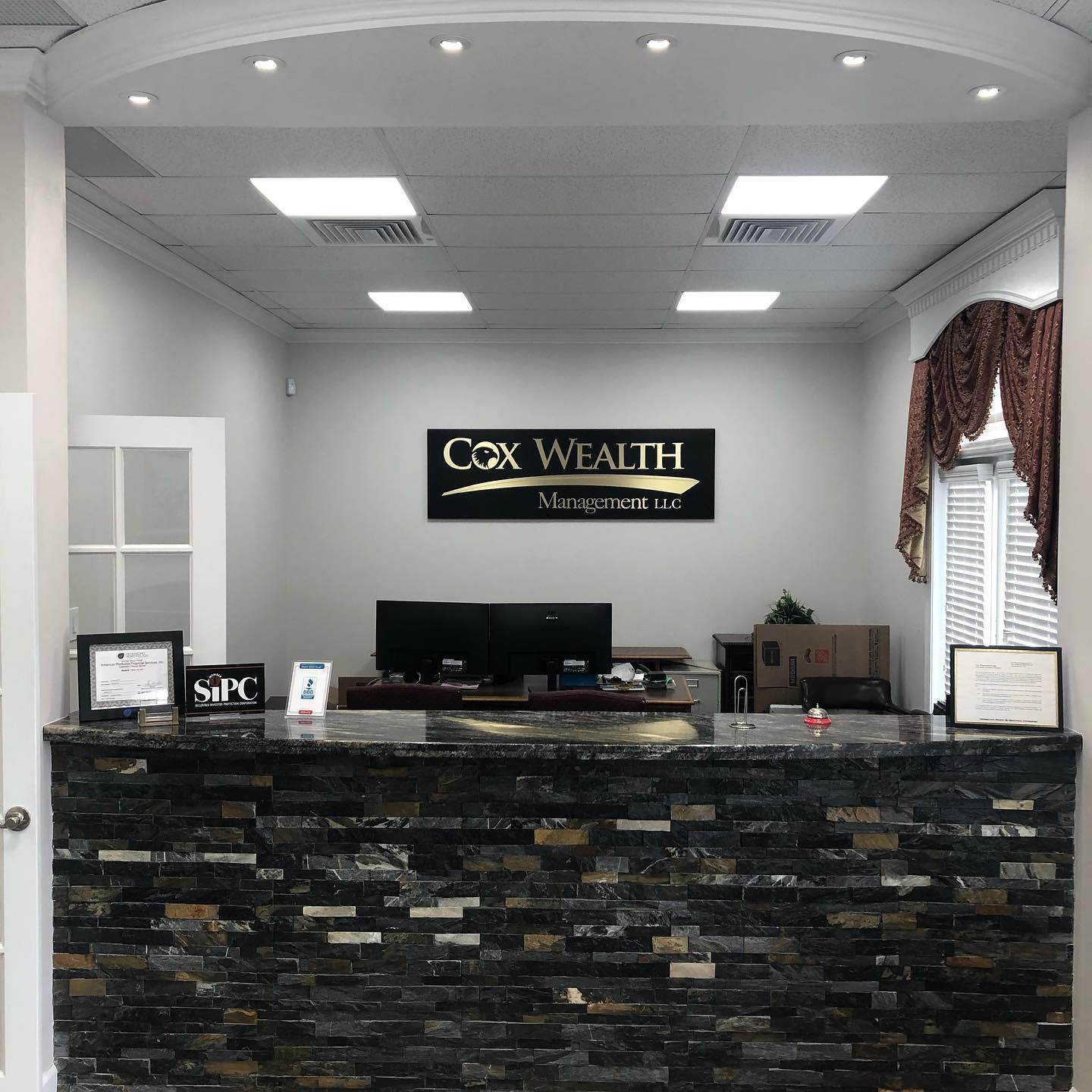 Reception desk for Cox Wealth Management. Dark stone facade, black and gold sign, and a white door.