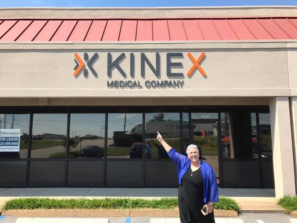 Woman points at Kinex Medical Company sign outside building.