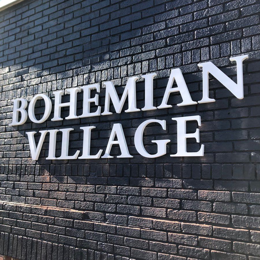 White "Bohemian Village" sign on black brick wall.