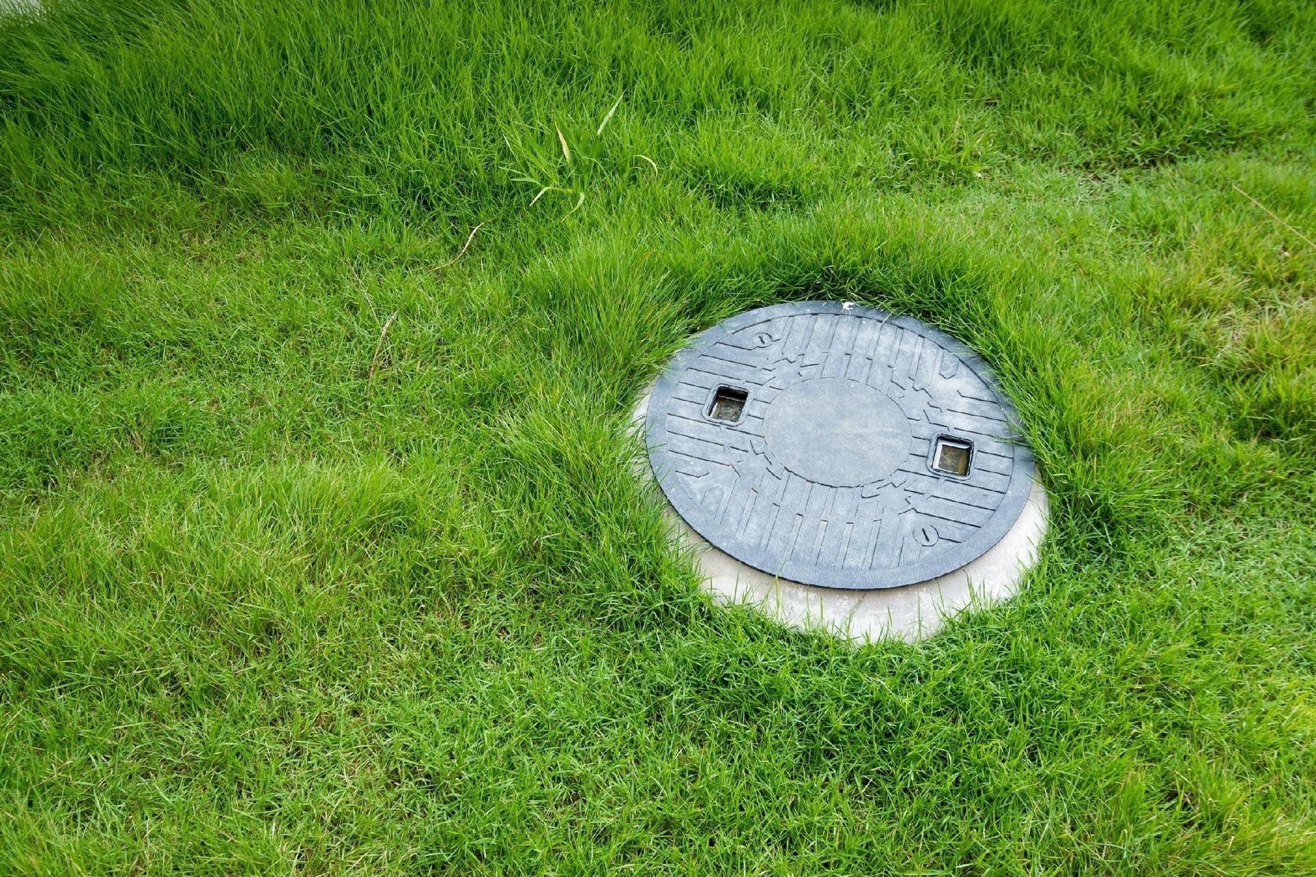 Round metal cover, set in green grass, presumably for access to an underground utility.